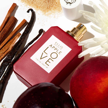 Apple Love 50ml bottle laying on white background with vanilla, sugar, apples and white flowers.