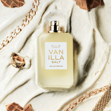 Vanilla Salt 50ml Eau De Parfum without cap in melted vanilla ice cream next to gold ring, gold bracelets, and pieces of ice cream cone.