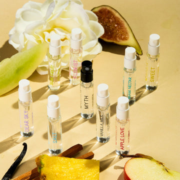 Dear Sky Eau De Parfum 1.5ml Vial, Miami Nectar Eau De Parfum 1.5ml Vial, Apple Love Eau De Parfum 1.5ml Vial, Salt Eau De Parfum 1.5ml Vial, Sun Fruit Eau De Parfum 1.5ml Vial, Florist Eau De Parfum 1.5ml Vial, Myth Eau De Parfum 1.5ml Vial, Sweet Eau De Parfum 1.5ml Vial, and Vanilla Milk Eau De Parfum 1.5ml Vial, on yellow background with fig, white flower, honeydew, vanilla bean, sandalwood, pineapple, and apple.