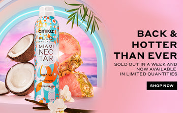 Amika x Ellis Brooklyn Miami Nectar Perk Up Dry Shampoo on pink pedestal with vanilla beans, coconut, pine pineapple, and flowers on white table against neon arch and pink sunset and palm leaves, on pink background with black text that reads "Back & Hotter Than Ever Sold Out In A Week And Now Available In Limited Quantities" and black rectangle with white text that reads "Shop Now".