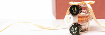 Three 50ml Eau De Parfum bottles stacked on each other, tied together with gold ribbon, in front of red box, on white background.