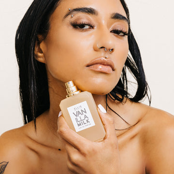 Model with brown hair holding open Vanilla Milk 50ml perfume bottle on a white background.