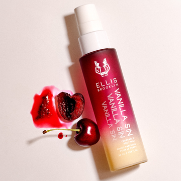 Vanilla Sin Hair And Body Fragrance Mist 50ml on pale pink background next  to cherries and cherry juice.