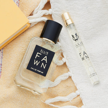 Fawn 50ml Eau De Parfum and Fawn 10ml Eau De Parfum Travel Spray on white tasseled towel, and yellow towel, next to yellow book.