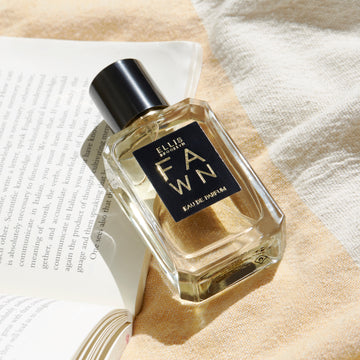 Fawn 50ml Eau De Parfum resting on open book page, on yellow and white towel.