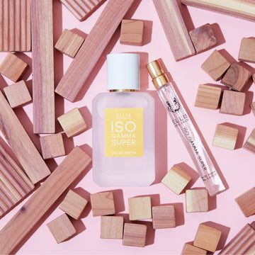 Iso Gamma Super 50ml Eau De Parfum and Iso Gamma Super 10ml Eau De Parfum Travel Spray next to square and rectangular wooden blocks, on pink background.
