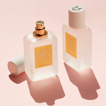 Two bottles of Iso Gamma Super 50ml Eau De Parfum, one with cap removed, on pink background.