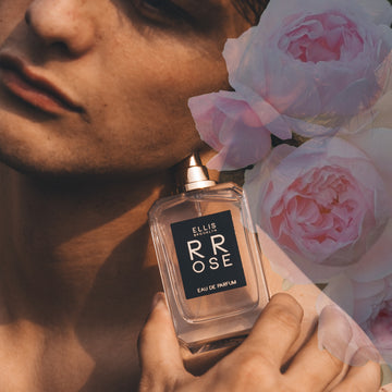 Model holding Rrose 50ml Eau De Parfum without cap against jaw with pink flower graphic in background.