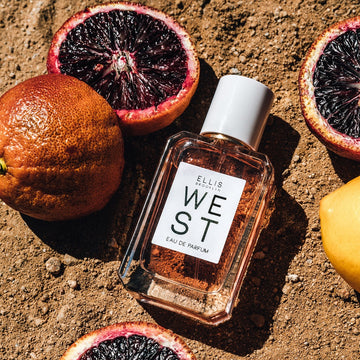 West 50ml Eau De Parfum on dirt next to blood oranges and lemon.