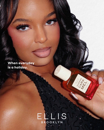 Model with brown, curled hair in a black, beaded halter tank top looks into camera while holding Queens Caramel Eau de Parfum 50ml on a white background with white text that reads "When everyday is a holiday." and "Ellis Brooklyn"