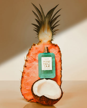 MIAMI NECTAR Eau de Parfum 50ml without cap on top of half of a coconut against half of a pink pineapple on a tan background