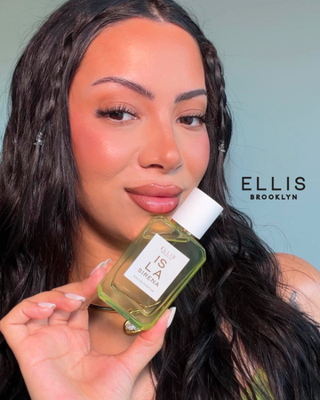 Woman with brown hair with braids holds ISLA SIRENA Eau de Parfum 50ml against a blue background with black text that reads "Ellis Brooklyn"