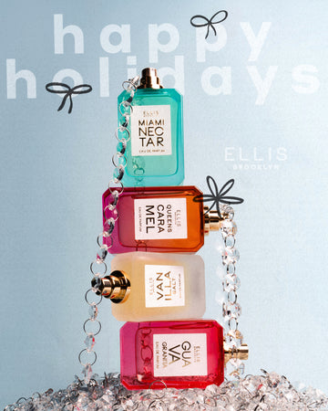 Miami Nectar 50ml Eau De Parfum without cap on top of Queens Caramel 50ml Eau De Parfum without cap on top of Vanilla Salt 50ml Eau De Parfum without cap on top of Guava Granita 50ml Eau De Parfum without cap, wrapped in beaded chain while resting on piled of beaded chain against blue background and white text that reads "Happy Holidays" with a black bow on the second 'p' in happy and the 'o' in holiday and "Ellis Brooklyn".