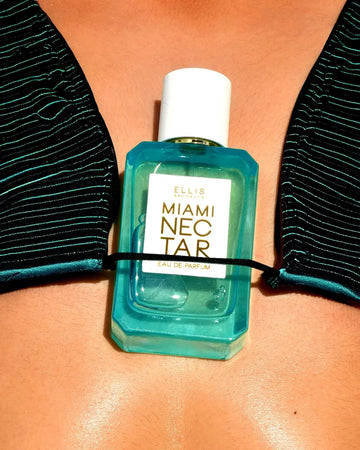 Miami Nectar 50ml Eau De Parfum tucked under middle of dark green metallic striped bikini top on model.