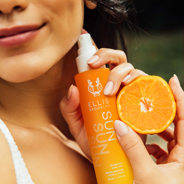 IMAGE 7: MODEL HOLDING SUN FRAGRANCE AND BODY MIST AND ORANGE