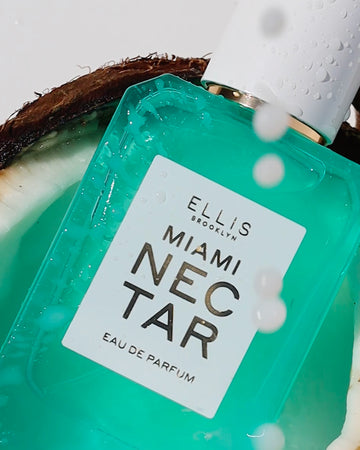 Closeup of MIAMI NECTAR Eau de Parfum 50ml covered in water droplets sitting in half of a coconut against a white background