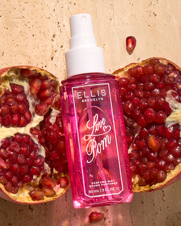 LOVE POM Perfume Mist 90ml without cap lays on two halves of a pomegranate on top of tan marble