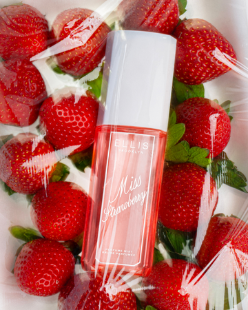 MISS STRAWBERRY Perfume Mist 90ml lays on strawberries on white surface all covered by clear plastic