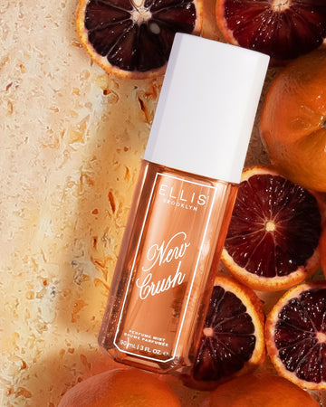 NEW CRUSH Perfume Mist 90ml lays on orange marble, sliced blood oranges, and clementines