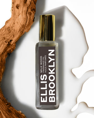 Milk Wood Fragrance Oil 15ml resting in milk next to piece of wood on white background. 