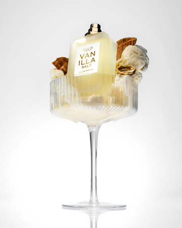 Vanilla Salt 50ml Eau De Parfum without cap in glass with vanilla ice cream, pieces of ice cream cone, and gold ring, on white background