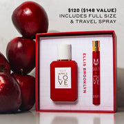 Apple Love Eau De Parfum Gift Set Box showing Apple Love 50ml Eau De Parfum and Apple Love 10ml Eau De Parfum Travel Spray on white table next to stack of red apples on white background with black text that reads "$120 ($148 value) includes full size & travel spray"