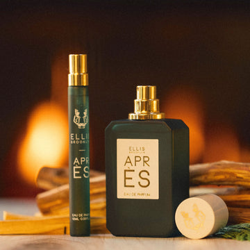 Après 10 ml de vaporisateur de voyage Eau de Parfum à côté de 50 ml d'Eau de Parfum avec le bouchon enlevé sur une table en bois avec des morceaux de bois et de petites feuilles vertes, avec du feu en arrière-plan.