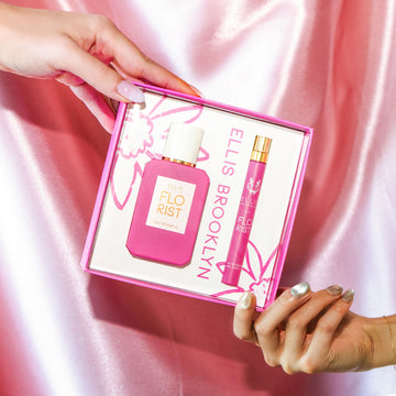 Modèle avec du vernis à ongles nude tenant le coin supérieur de la boîte du coffret cadeau Florist Eau De Parfum montrant Florist 50 ml Eau De Parfum et Florist 10 ml Eau De Parfum vaporisateur de voyage, et modèle avec du vernis à ongles gris irisé tenant le coin inférieur de la même boîte, sur fond de satin rose.
