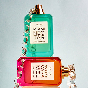 Metal and diamond chain resting on top of Miami Nectar 50ml Eau De Parfum without cap that is stacked on top of Queens Caramel 50ml Eau De Parfum without cap, on light grey background.