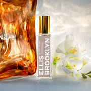 Huile parfumée Blond Musk (15 ml) placée à côté d'un bloc d'ambre et de fleurs blanches, sur fond blanc.