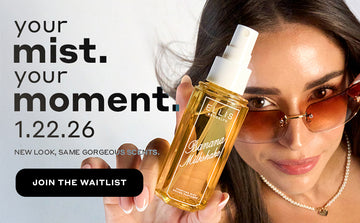 Model with brown hair wearing brown sunglasses and a pearl necklace looks up at the camera while holding BANANA MILKSHAKE 90ml perfume mist without a cap, with black text that reads "your mist. your moment. 1.22.26. New Look, Same Gorgeous Scents." and a black oval with white text that reads "Join The Waitlist" all on a gray background.