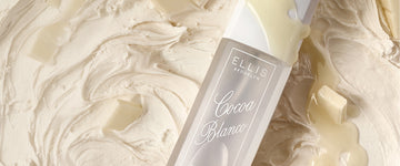 Closeup of COCOA BLANCO perfume mist 90ml laying on vanilla icing, chunks of white chocolate, and a drizzle of white chocolate across the bottle. 