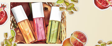 NEW CRUSH Perfume Mist 90ml, LOVE POM Perfume Mist 90ml, and FOREVER PISTACHIO Perfume Mist 90ml in basket filled with pomegranates and blood oranges on a light yellow background overlaid with images of drawn pistachios, sliced pomegranates, and sliced blood oranges outlined in white