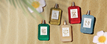 MIAMI NECTAR Eau de Parfum 50ml without cap, ISLA SIRENA Eau de Parfum 50ml without cap, VANILLA SALT Eau de Parfum 50ml without cap, GUAVA GRANITA Eau de Parfum 50ml without cap, and SALT Eau de Parfum 50ml without cap next to white and yellow flowers all on tan sand with green palm leaves in the corner
