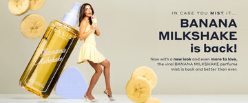 Model with brown hair in yellow dress and yellow heels drinks a yellow milkshake in a glass cup with a straw, faces to the side and holds up with her back a life size bottle of BANANA MILKSHAKE Perfume Mist without a cap next to it's cap with black text that reads "In case you mist it... BANANA MILKSHAKE is back! Now with a new look and even more to love, the viral BANANA MILKSHAKE perfume mist is back and better than ever." on a gray background with life size banana slices