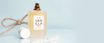 Vanilla Salt 50ml Eau De Parfum with cap removed, crystal bow, and strand of pearls on light blue background.
