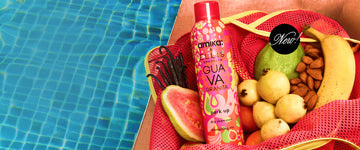 Amika x Ellis Brooklyn GUAVA GRANITA Perk Up Dry Shampoo in pink and yellow mesh bag with guavas, vanilla beans, almonds, a banana, and oranges on a brown table next to a blue pool with white text in black circle that reads "New!"