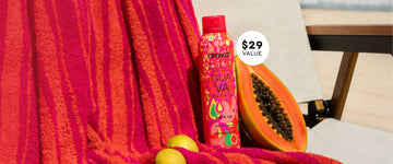 Amika x Ellis Brooklyn GUAVA GRANITA Perk Up Dry Shampoo between guavas and sliced papaya on a white beach chair covered in a pink and orange striped towel on the beach with a white circle with black text that reads '$29 Value'