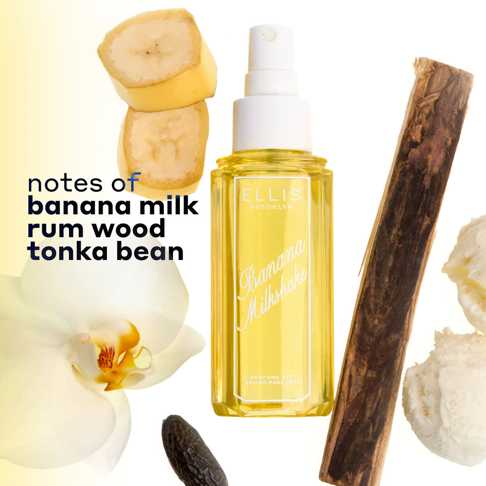 BANANA MILKSHAKE Perfume Mist 240ml without a cap surrounded by 2 slices of banana, a piece of rum wood, 2 scoops of vanilla ice cream, a tonka bean, and a flower on a white and yellow ombré background with black text that reads "notes of banana milk, rum wood, tonka bean"