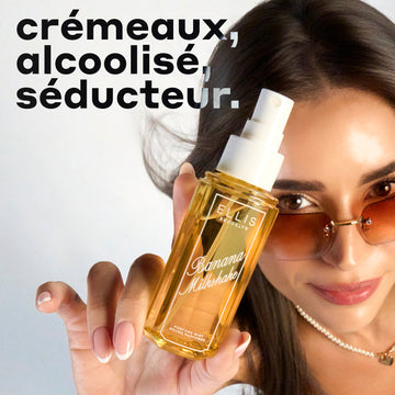 Un mannequin aux cheveux bruns portant des lunettes de soleil marron, une robe jaune et un collier de perles regarde l'appareil photo tout en tenant un spray de parfum BANANA MILKSHAKE 90 ml sans bouchon sur un fond dégradé bleu et blanc avec du texte noir, blanc et bleu qui dit « crémeux, alcoolisé, séducteur ».