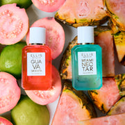 Guava Granita 7.5ml Eau De Parfum Mini Dabber resting on cut guavas next to Miami Nectar 7.5ml Eau De Parfum Mini Dabber resting on slices of pink pineapple, on white background.