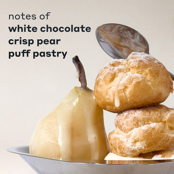 COCOA BLANCO fragrance notes displayed with a white chocolate-drizzled pear and two powdered puff pastries on a silver tray, with a spoon behind them and black text that reads "notes of white chocolate, crisp pear, puff pastry" on a cream background.