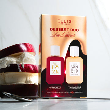 Dessert Duo box standing next to sliced red apple and vanilla ice cream stacked on one another, behind spoon, on marble background. 
