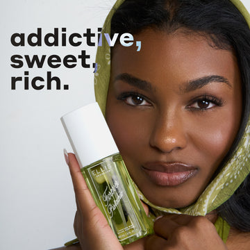 Woman with black hair wearing a green scarf on her head and holding a bottle of FOREVER PISTACHIO Perfume Mist 90ml against her cheek on a white background with black and white text that reads "addictive, sweet, rich."