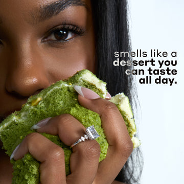 Woman with black hair wearing a diamond ring and holding green cake with white icing against a white background with black and gray text that reads "smells like a dessert you can taste all day."