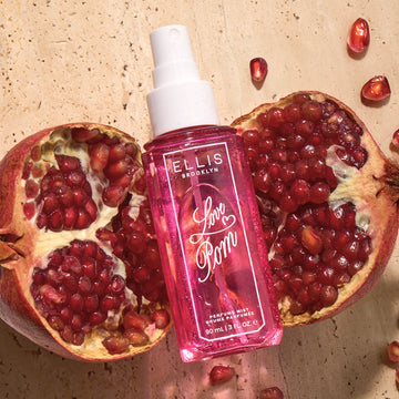 Brume parfumée LOVE POM 90ml sans bouchon posée sur deux moitiés de grenade sur un marbre beige