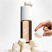 MARSHMALLOWS Perfume Mist 240ml with a marshmallow sitting on the cap, sitting on a pile of marshmallows and a hand grabbing a marshmallow from the pile on a white background