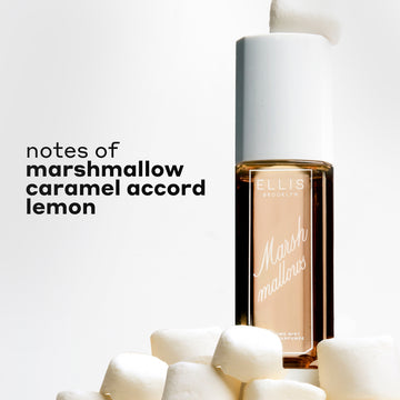 MARSHMALLOWS Perfume Mist 240ml with a marshmallow sitting on the cap, sitting on a pile of marshmallows with black text that reads "notes of marshmallow, caramel accord, lemon" on a white background