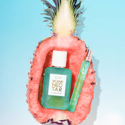 MIAMI NECTAR Eau de Parfum 50ml et MIAMI NECTAR Eau de Parfum 10ml placés à l'intérieur de la moitié d'un ananas rose sur fond bleu