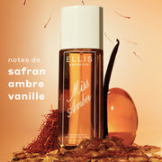 Bouteille de brume parfumée Miss Amber de 240 mL posée avec une gousse de vanille, du safran rouge et des pierres de couleur ambre autour, avec du texte à gauche indiquant « notes de safran, ambre, vanille ».